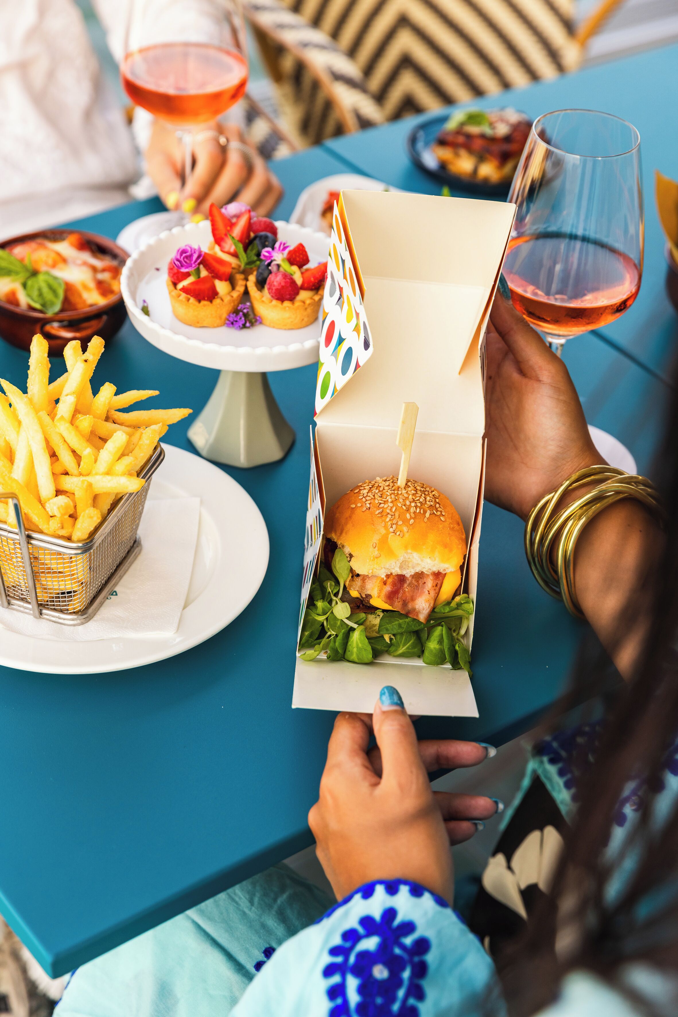 A dining table with food items, a drink, and a person holding a burger box.