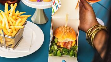 A dining table with food items, a drink, and a person holding a burger box.