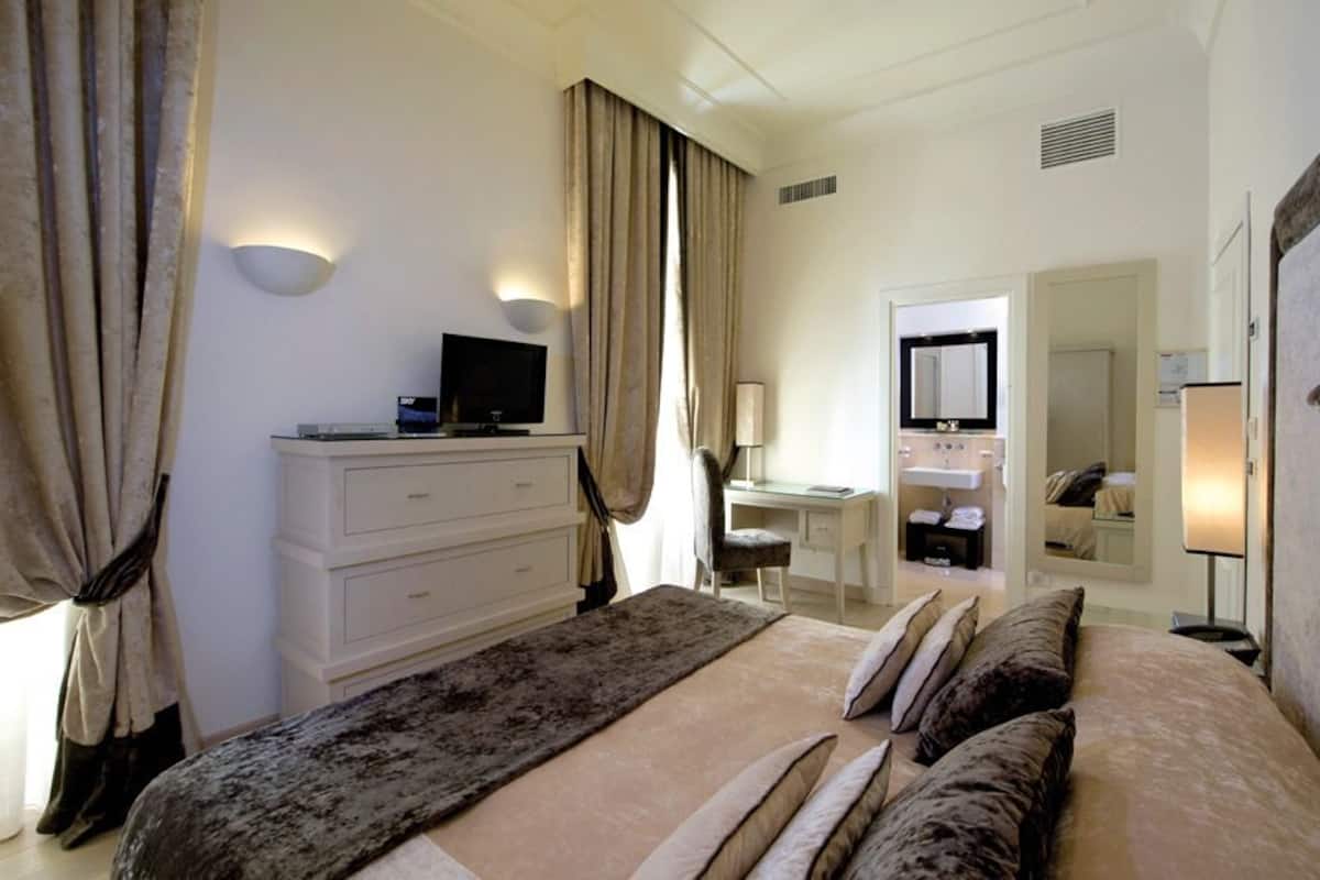 A hotel room with a bed, a desk, a television, and a bathroom mirror.