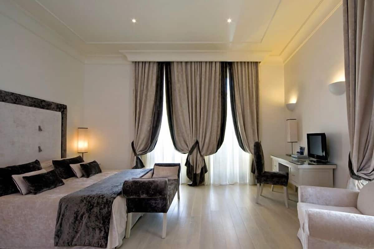 A hotel room with a large bed, a desk with a computer, a chair, and a TV.