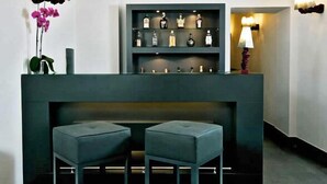 A reception area with a dark counter, two grey cushioned stools, a shelf with various bottles, and wall-mounted lamps. - Albergo Palazzo Decumani (Naples)