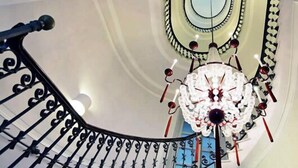 A spiral staircase with ornate black railings and a decorative chandelier at the top. - Albergo Palazzo Decumani (Naples)