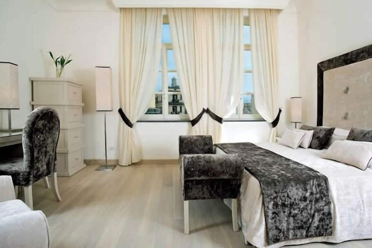 A modern bedroom with a bed, two chairs, a desk, and a window with curtains.