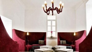A modern lounge area with a chandelier, red upholstered seating, and a central table. - Albergo Palazzo Decumani (Naples)
