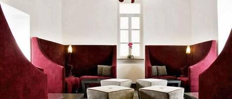 Un área de descanso moderna con candelabro, asientos tapizados en rojo y una mesa central.