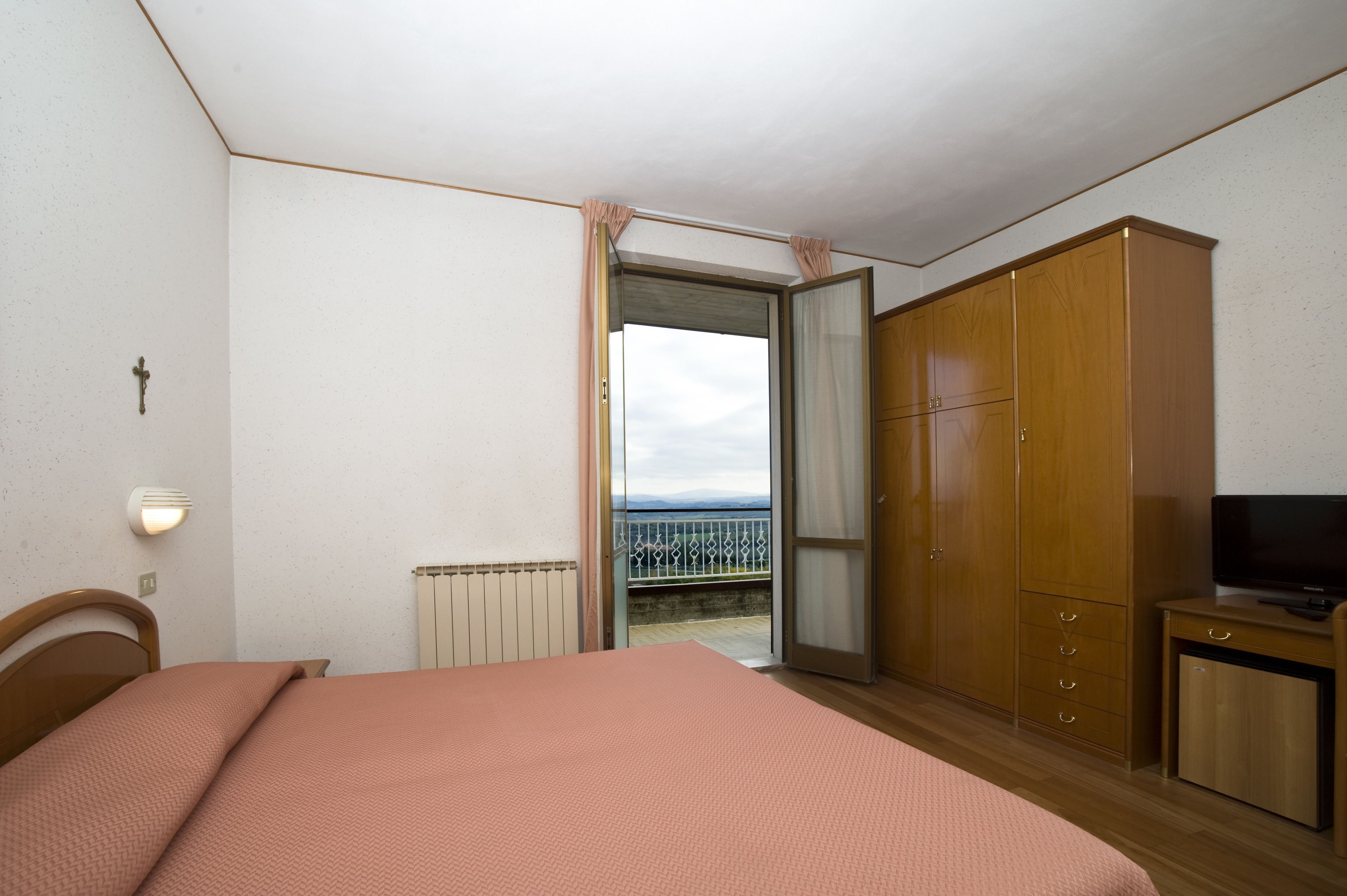 Quarto com cama, guarda-roupa, televisão e varanda com vista.