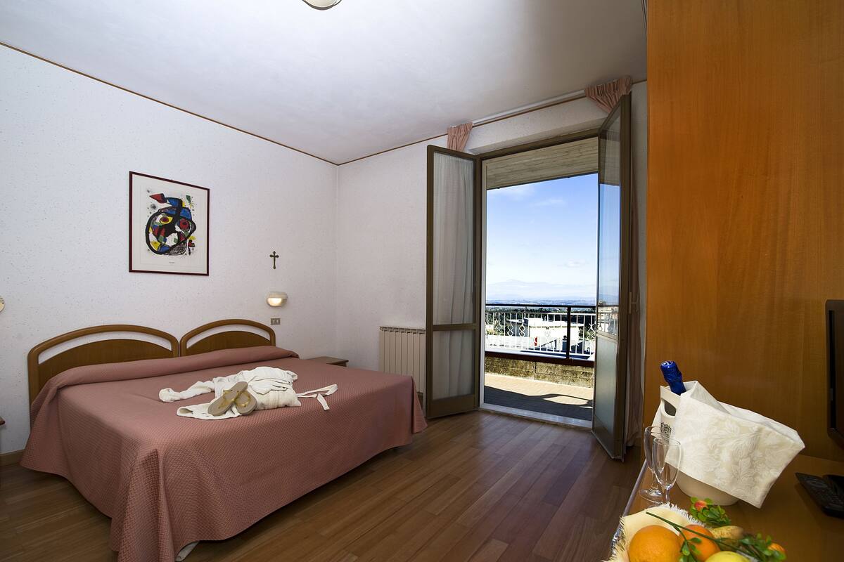 Ein Hotelzimmer mit Bett, einem Bild an der Wand und einem Balkon mit Blick.