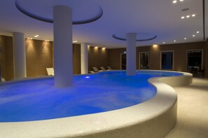 A modern indoor pool with a blue-lit water feature, surrounded by white pillars and a neutral-toned interior.