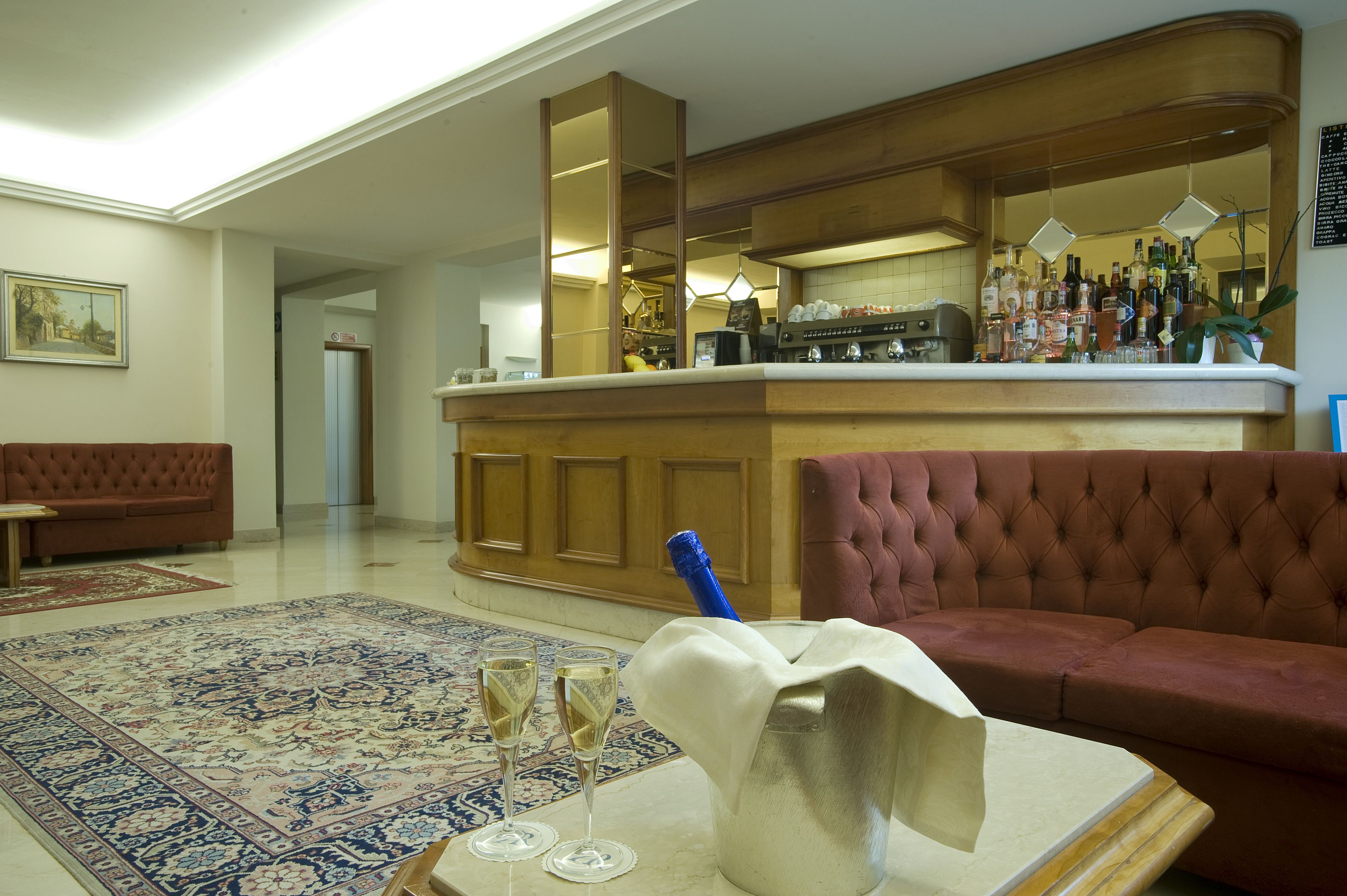 Amplia sala de estar con un tapete grande y ornamentado, un sofá capitonado y una zona de bar con diferentes botellas y vasos.