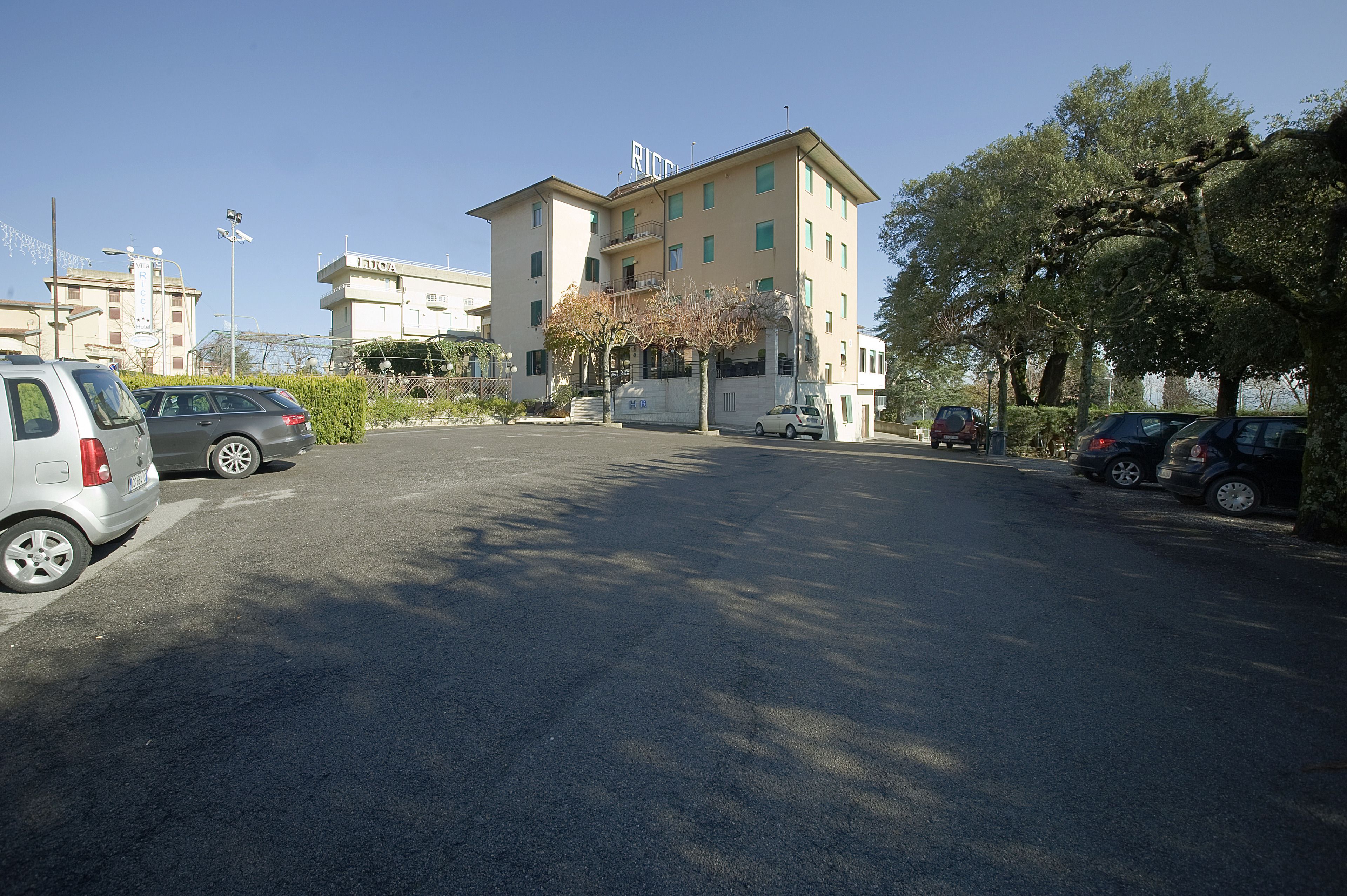 Un estacionamiento con varios coches y un edificio con la leyenda "RICO" al fondo.