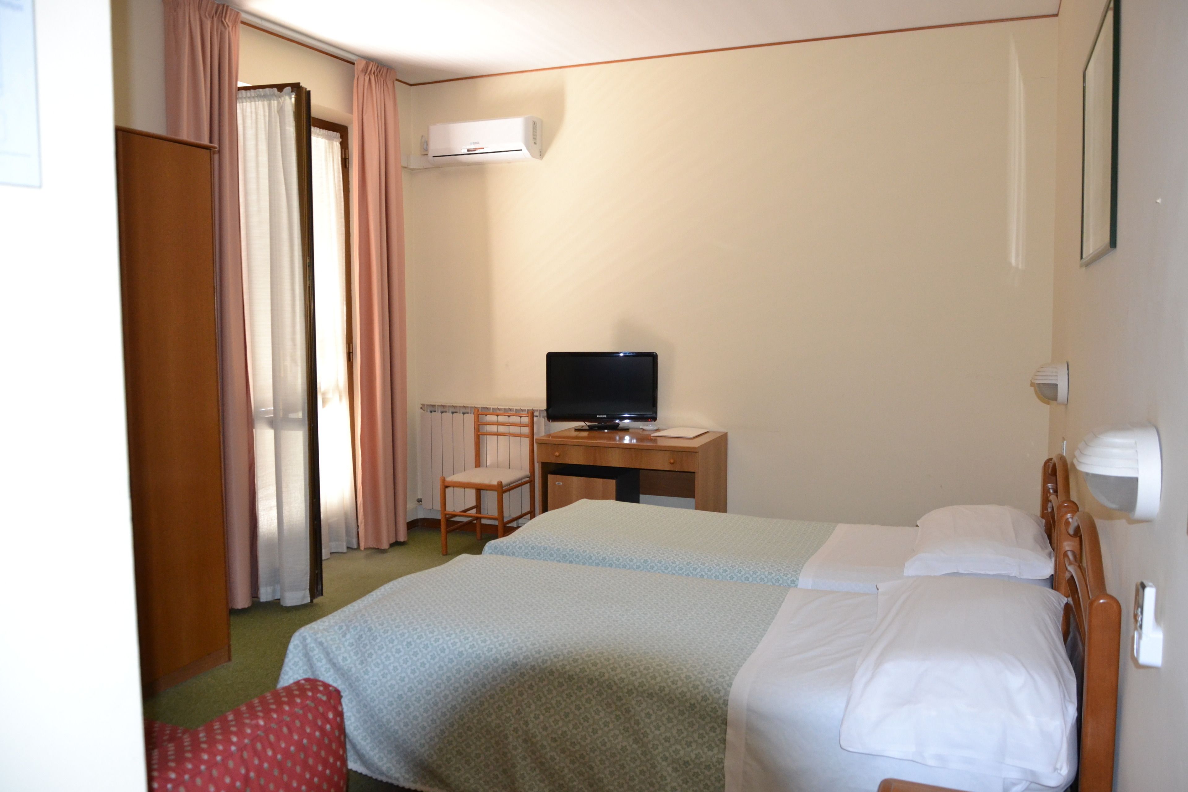 Een hotelkamer met een bed, een bureau met een televisie en een raam met gordijnen.