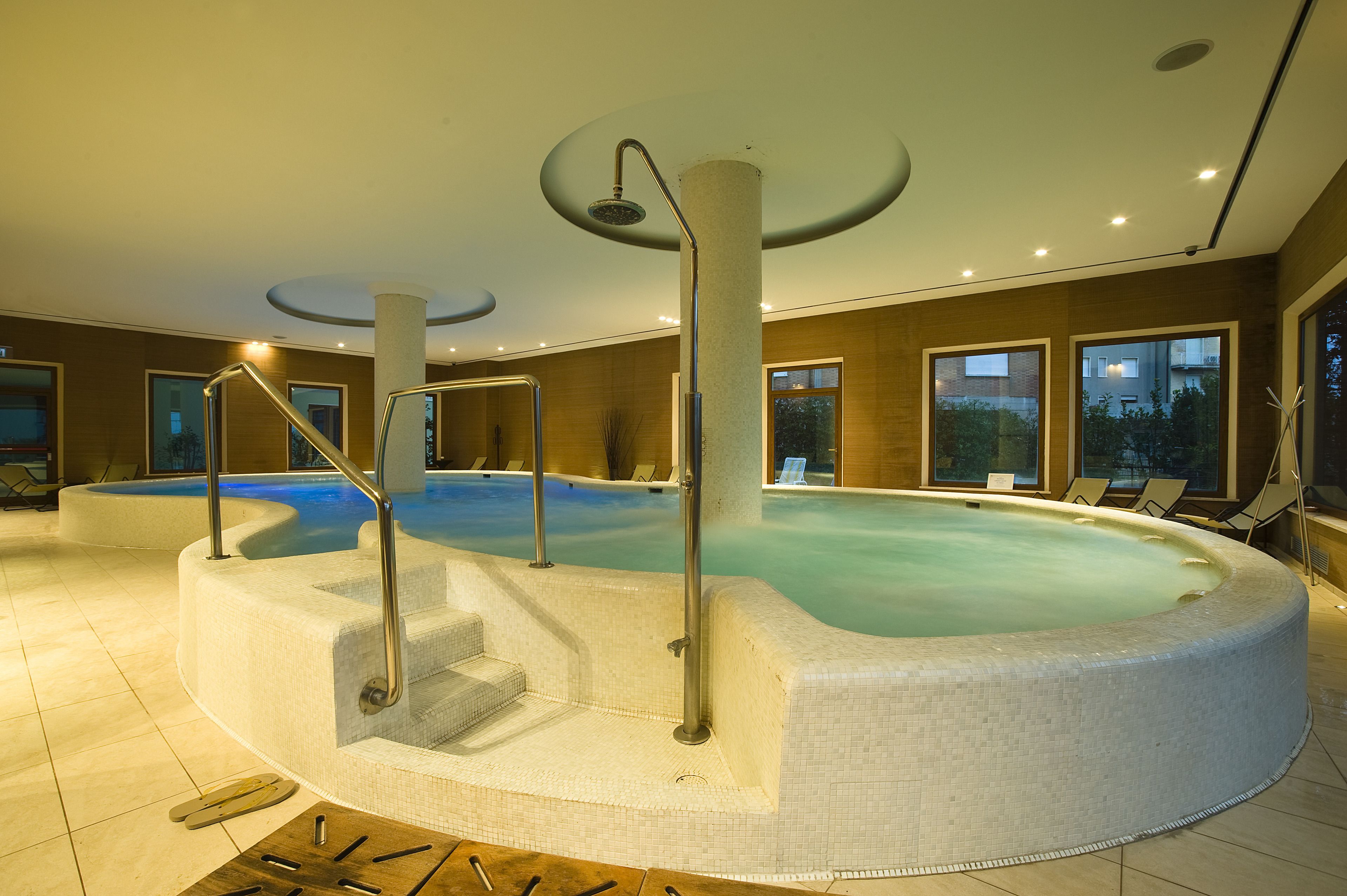 A hot tub with steps and railings, surrounded by lounge chairs and a view of buildings outside.