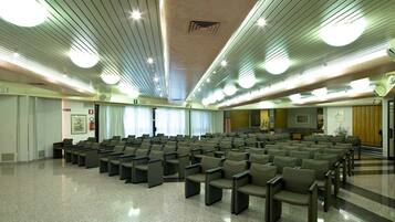 Uma sala de conferências com fileiras de cadeiras, piso lustroso e teto com luminárias lineares.