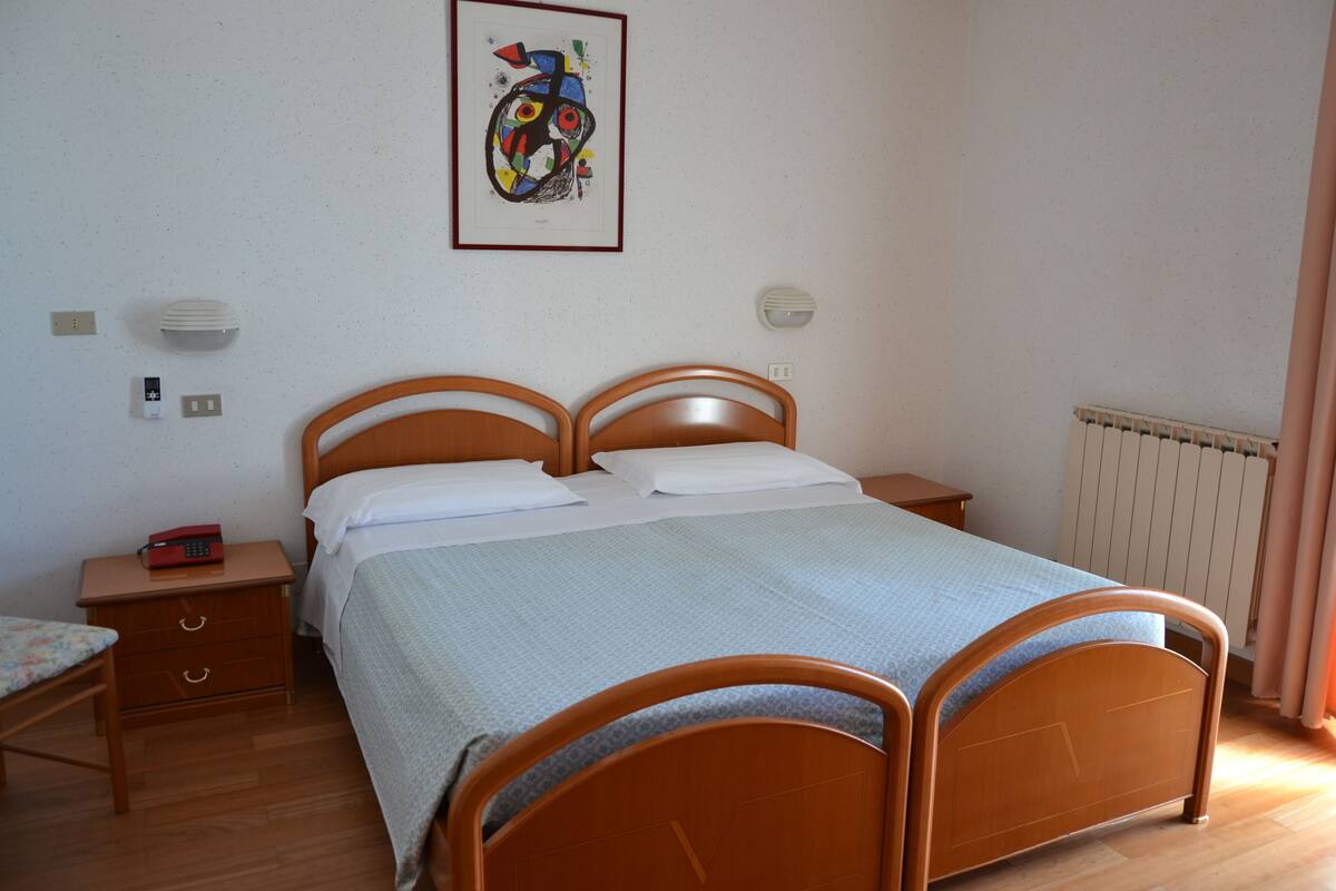 Ein Schlafzimmer mit einem hölzernen Bett, einem Nachttisch, einer Wandleuchte und einem gerahmten abstrakten Gemälde.