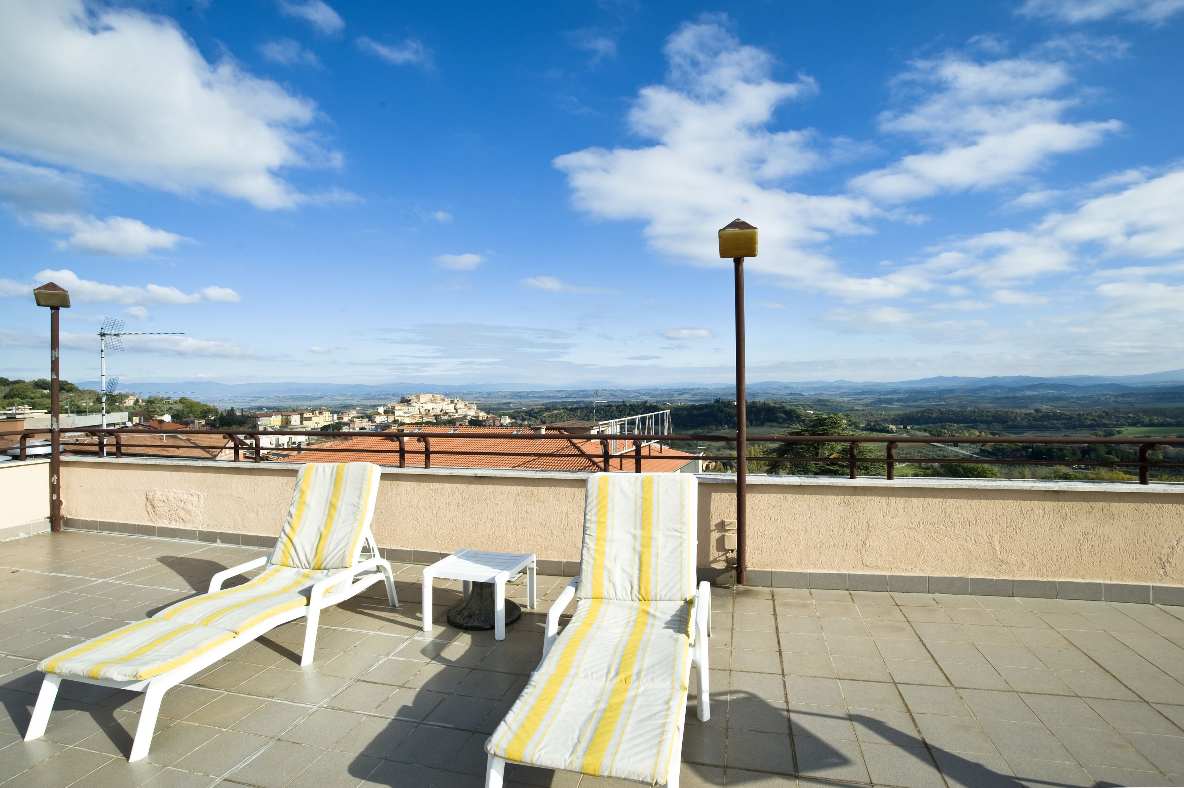 Une terrasse sur le toit, avec deux chaises longues à rayures et une petite table, d’où l’on peut admirer un paysage pittoresque avec des bâtiments visibles au loin.
