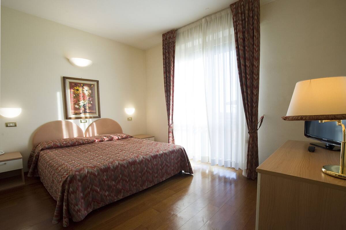 Ein Hotelzimmer mit einem Bett, einem Schreibtisch mit Lampe, einem Fernseher und einem Bild an der Wand.