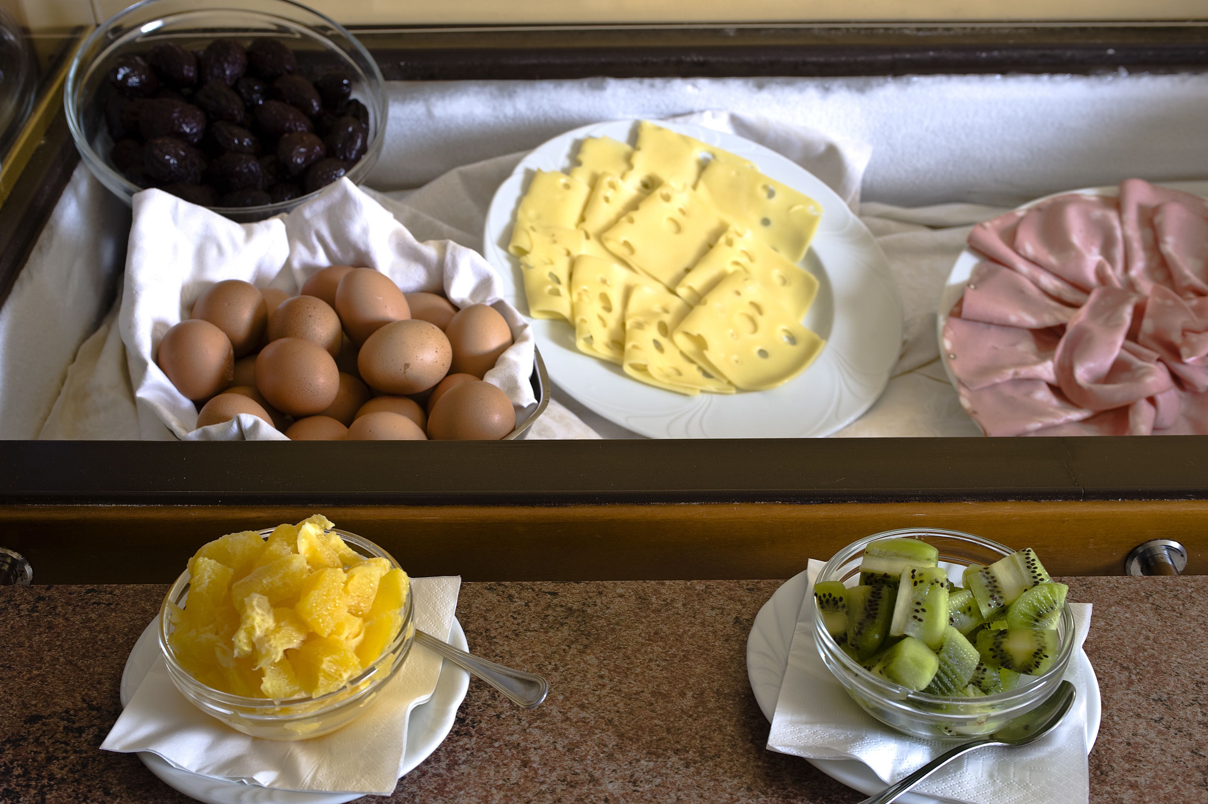 A breakfast tray with eggs, cheese, ham, and fruit.