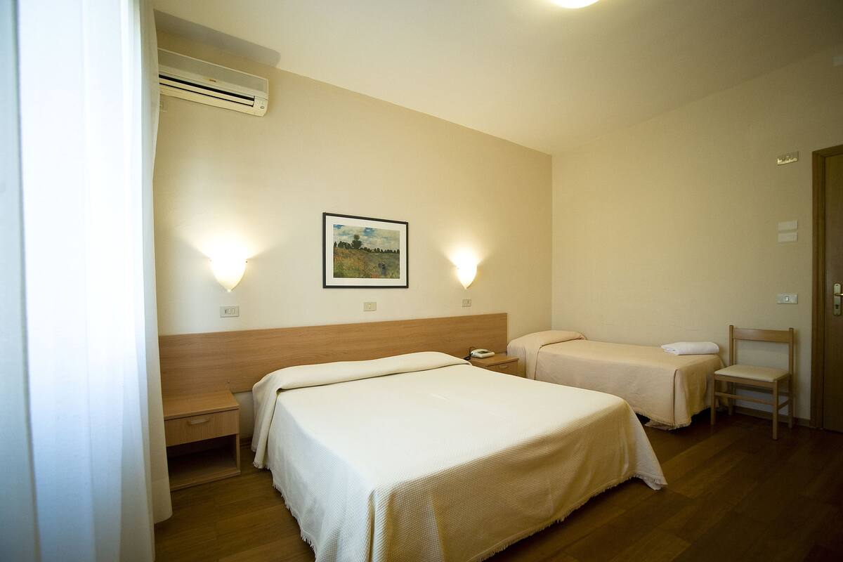 Ein Hotelzimmer mit zwei Betten, einem Holzkopfende, einem Nachttischchen mit Telefon, einem Sessel und einem Bild an der Wand.