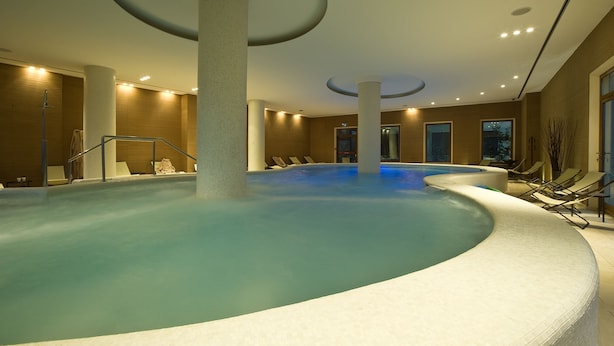 Una piscina interior de disseny corbat, envoltada de gandules i un sostre modern amb il·luminació empotrada.
