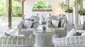 Un espacio de estar al aire libre cubierto con mobiliario de mimbre y una mesa de cristal central.