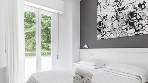 Habitación de hotel con una cama, cortinas blancas, un ventanal grande y un cuadro abstracto en blanco y negro en la pared.