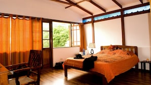A bedroom with a wooden bed, a chair, a desk, and a window with curtains.