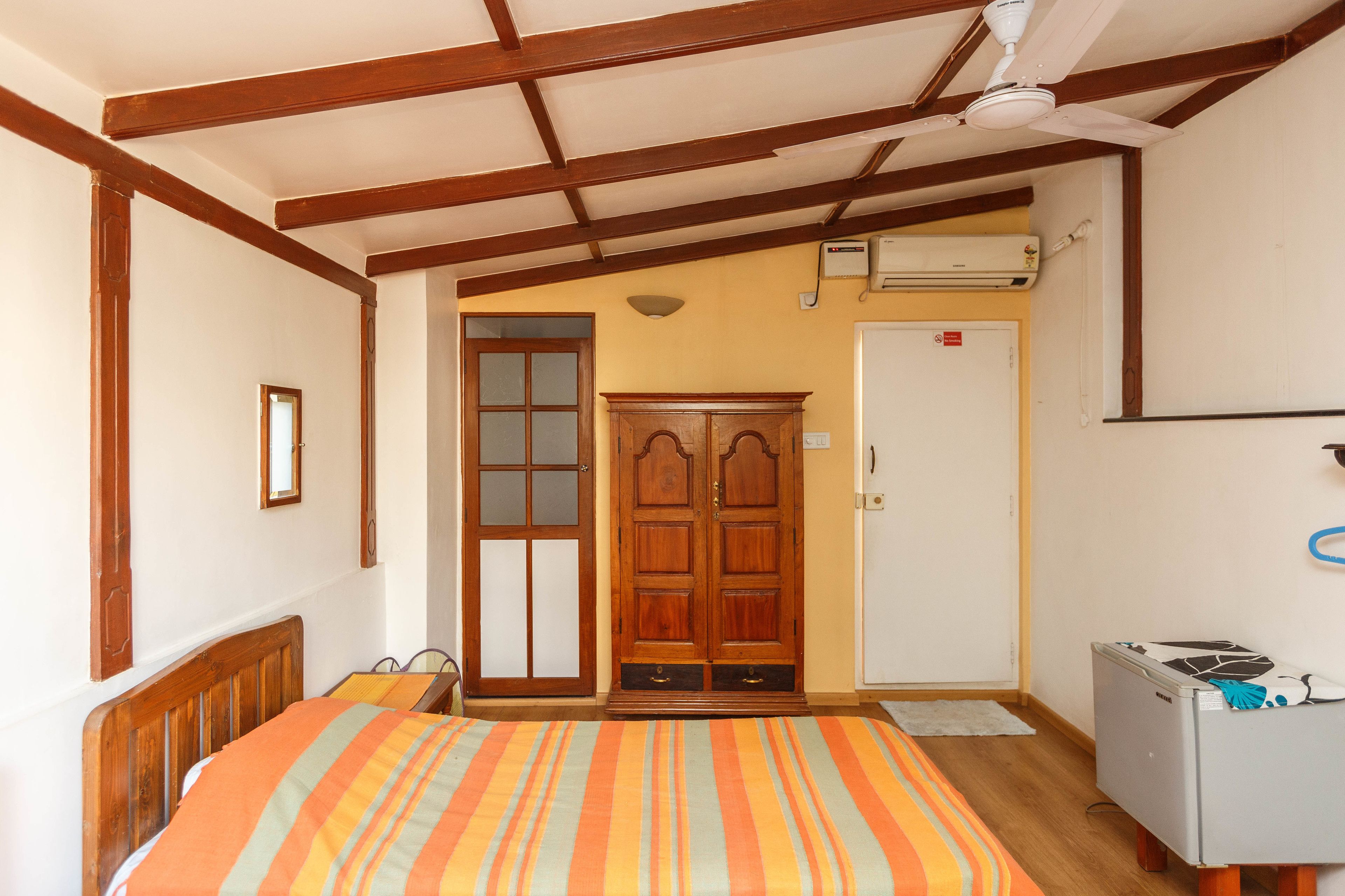 Um quarto com uma cama, um guarda-roupa, uma porta e um frigorífico pequeno.