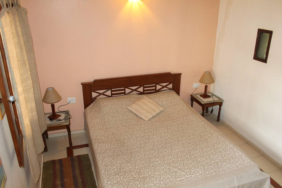 A bedroom with a bed, two bedside lamps, a nightstand, a small table, and a wall-mounted picture.
