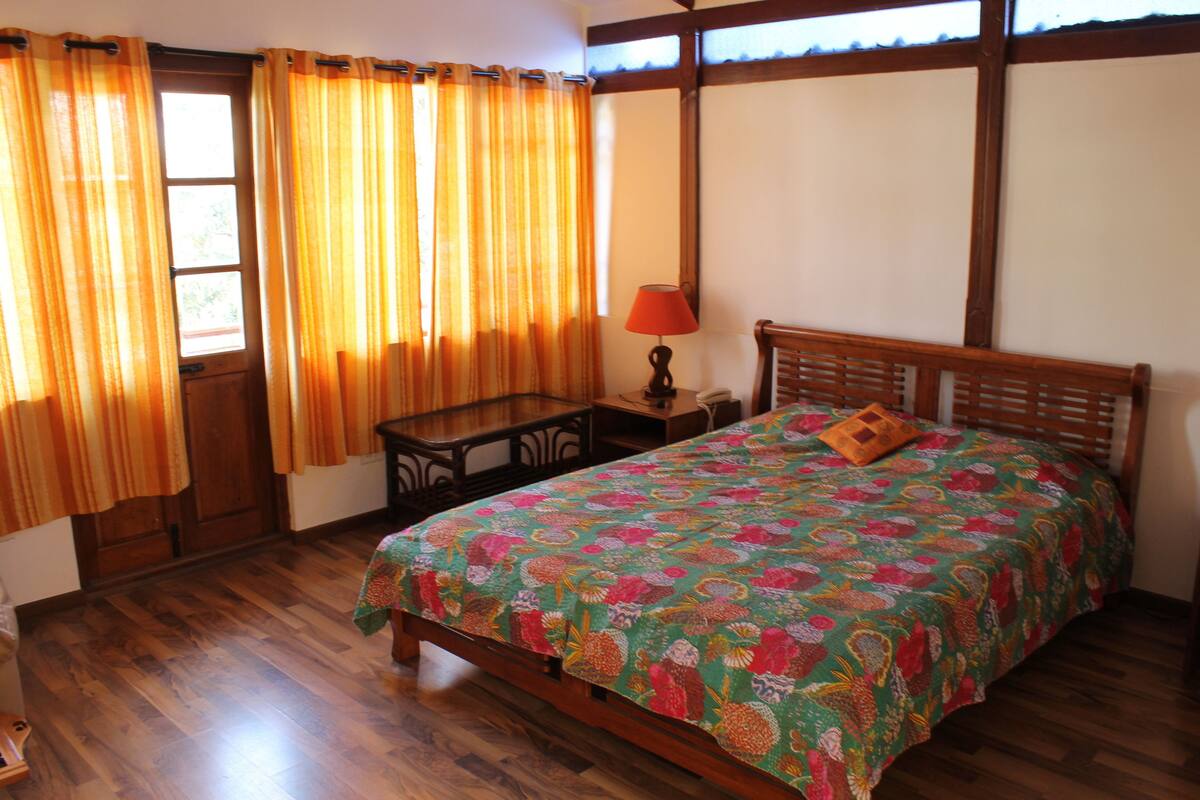 A bedroom with a wooden bed, a nightstand, a lamp, and a window with curtains.