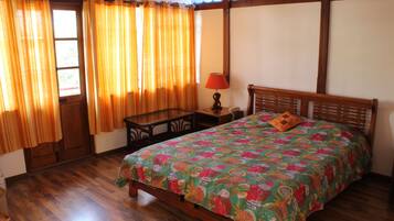 Un dormitorio con una cama de madera, una mesita de noche, una lámpara y un ventanal con cortinas.