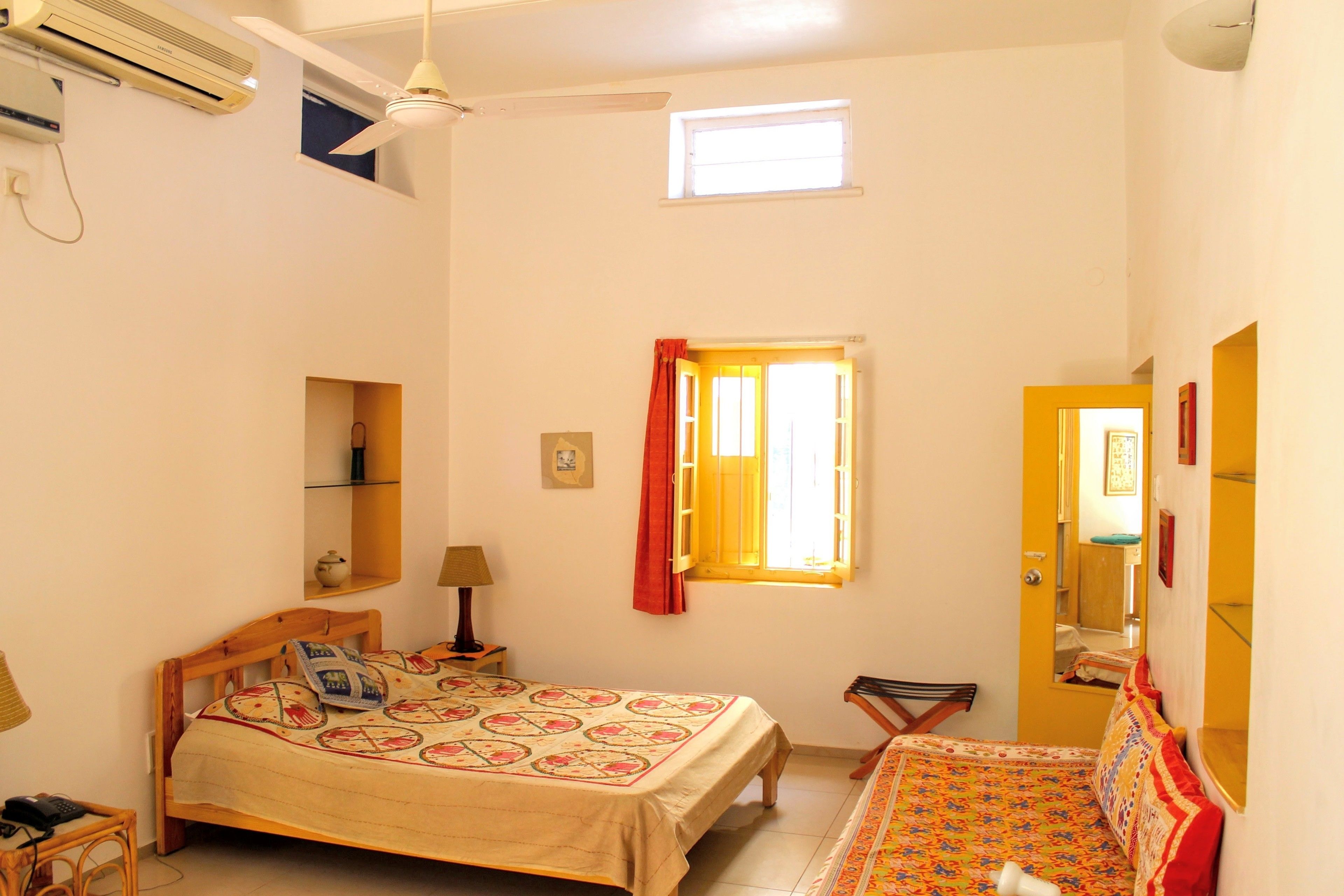 Un dormitorio con cama, una silla, una mesita, una ventana con cortinas y un espejo.