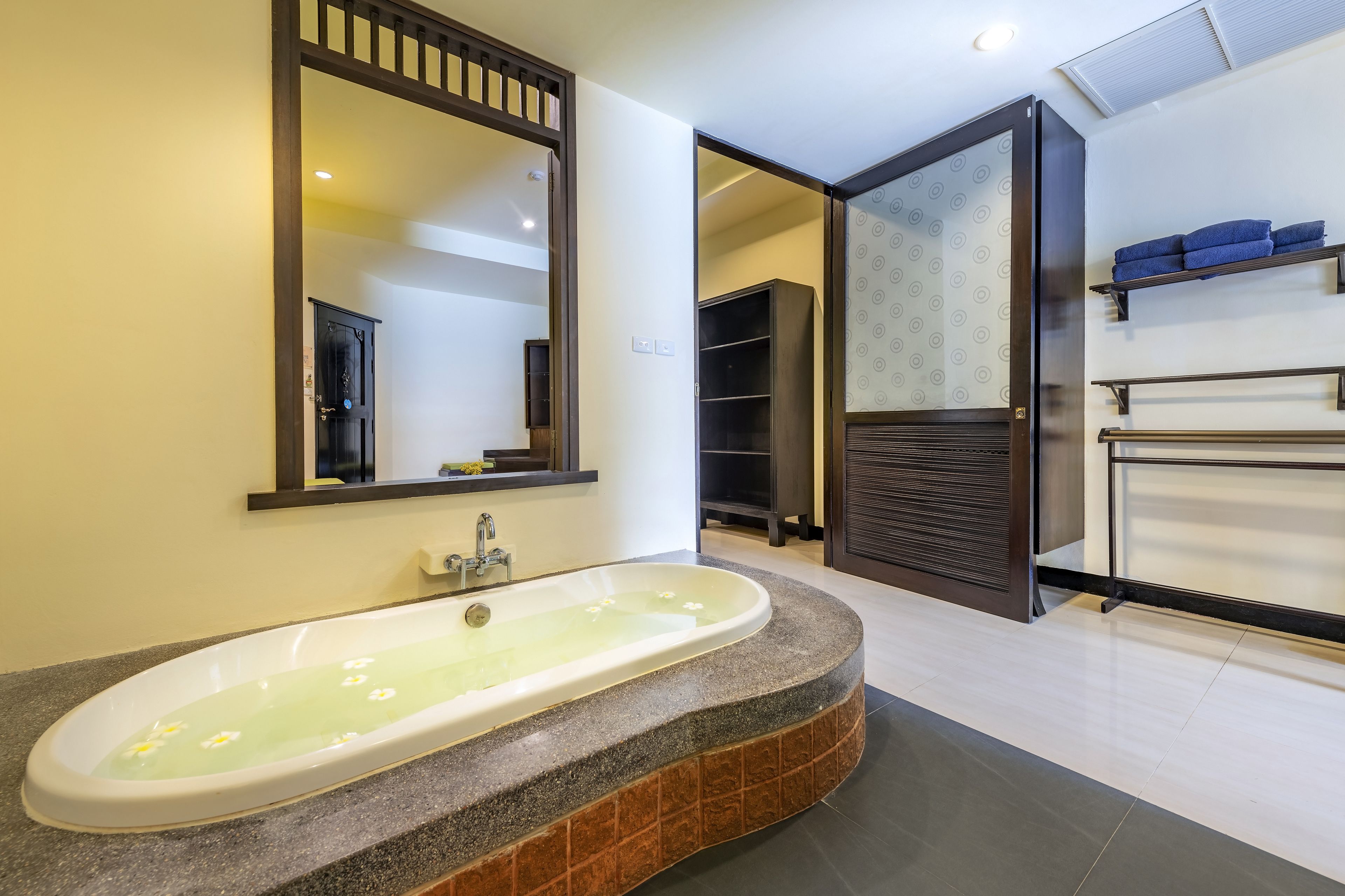A modern bathroom with a freestanding bathtub, a large mirror, and built-in shelving with towels.