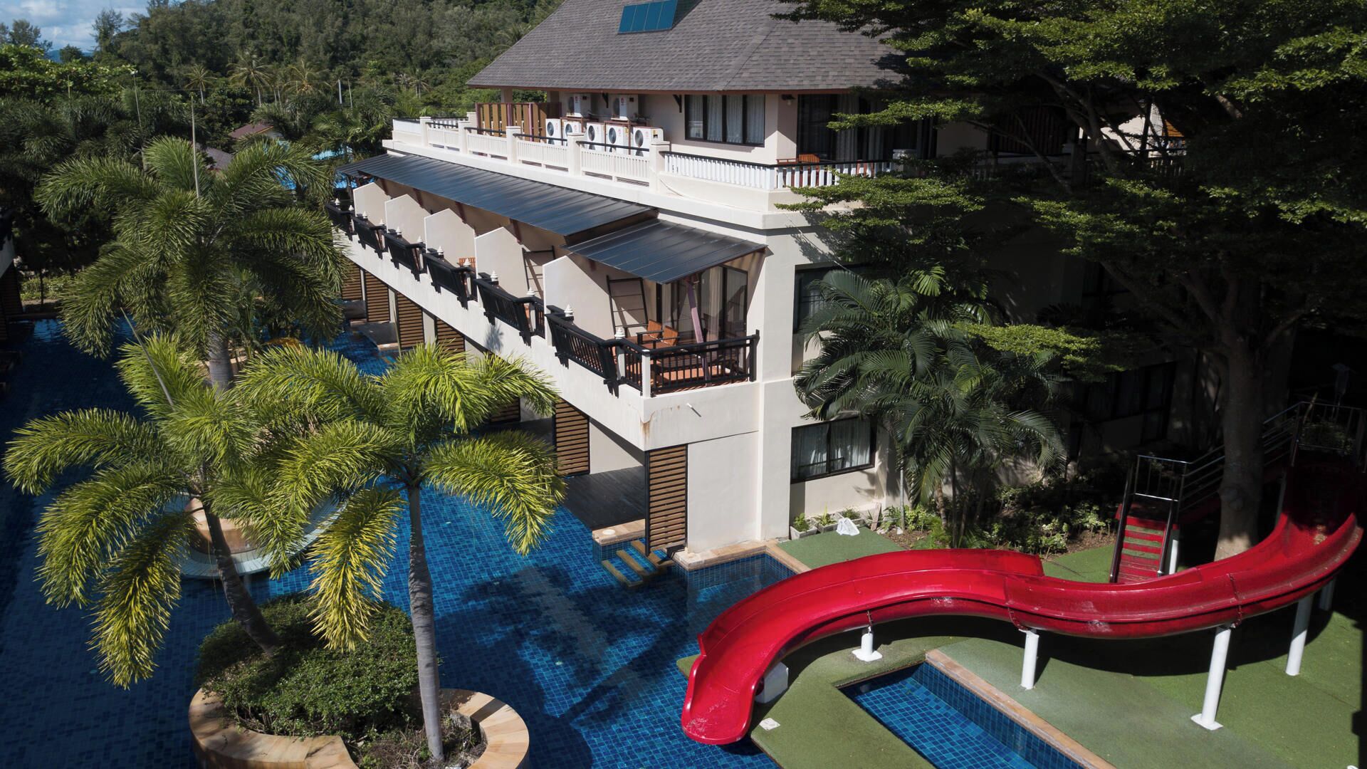 A resort with a pool, a red slide, and a building with a balcony.