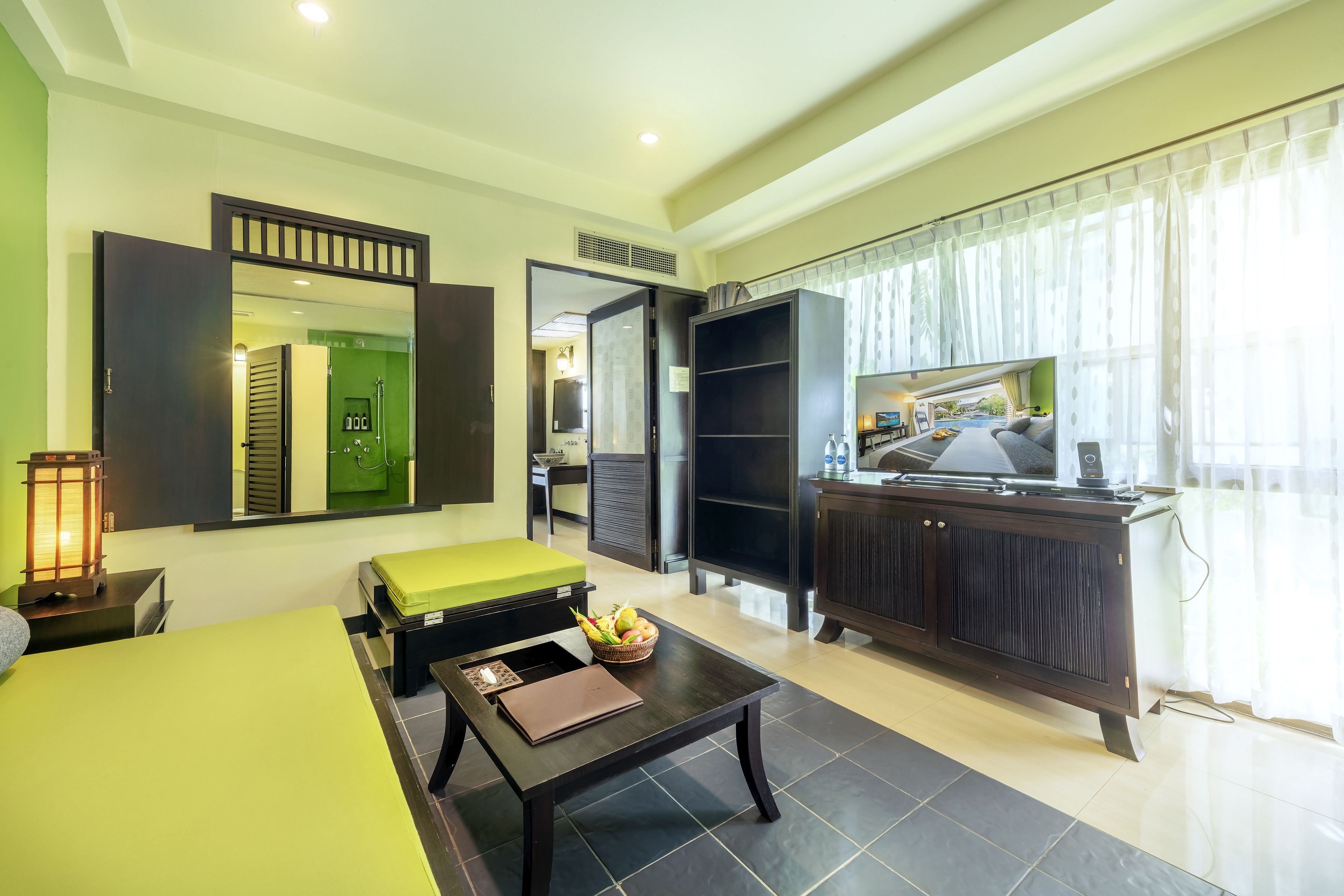 Habitación de hotel con cama, escritorio, silla, televisor, armario y baño visible a través de una puerta abierta.