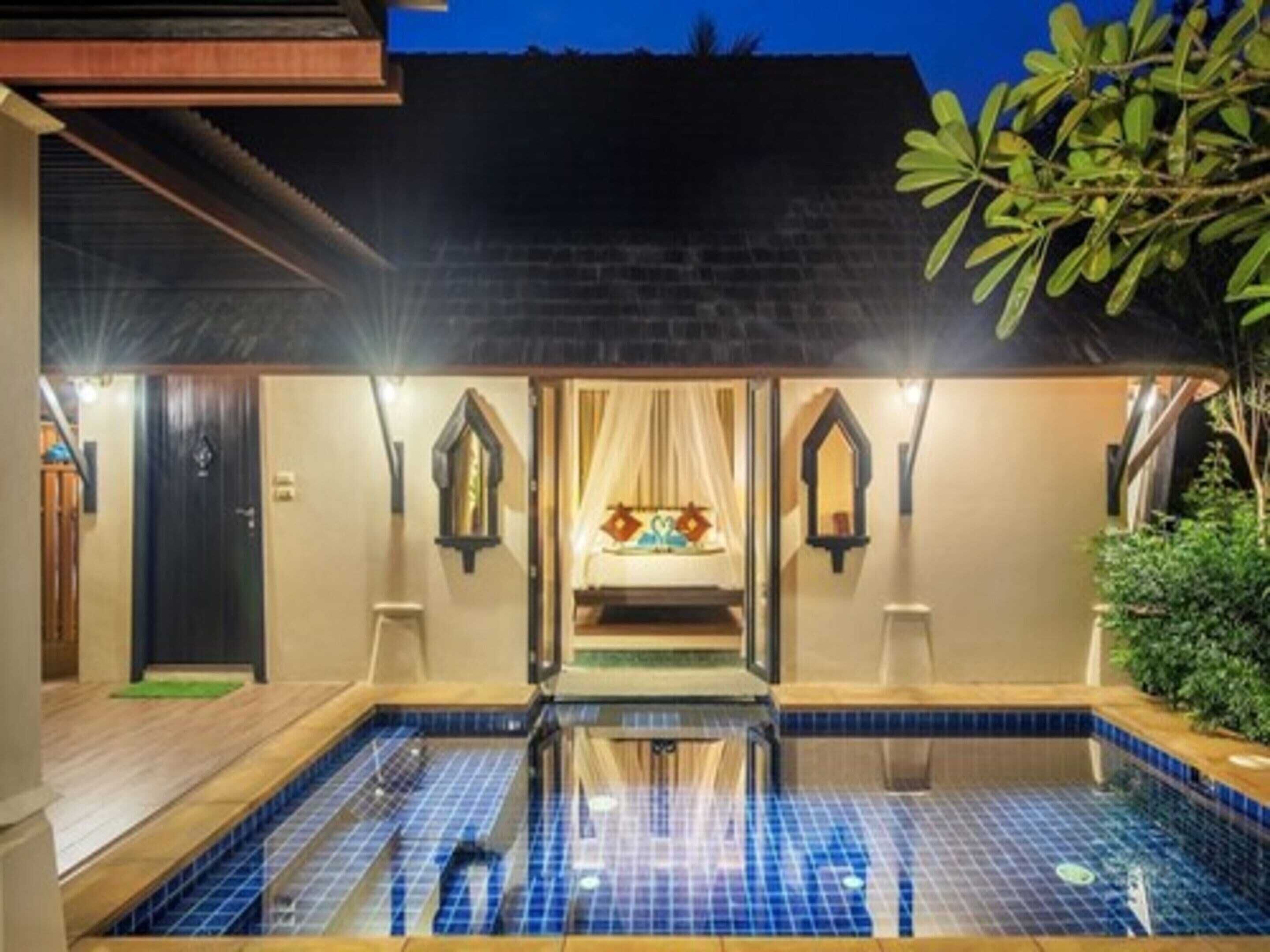 A pool area with a tiled floor, a bed with a canopy, and a small garden with a tree.