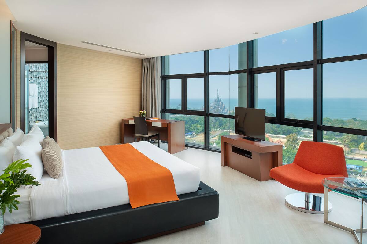 A modern hotel room with a large bed, a desk, a chair, and a TV.