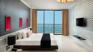 A modern hotel room with a large bed, a TV, and a balcony with a view of the sea.