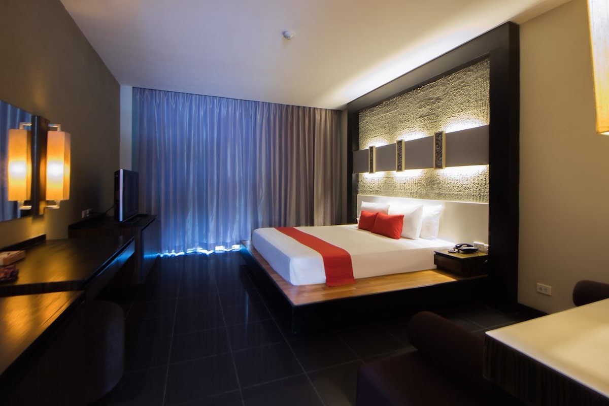 A modern hotel room with a large bed, a desk, and a TV.