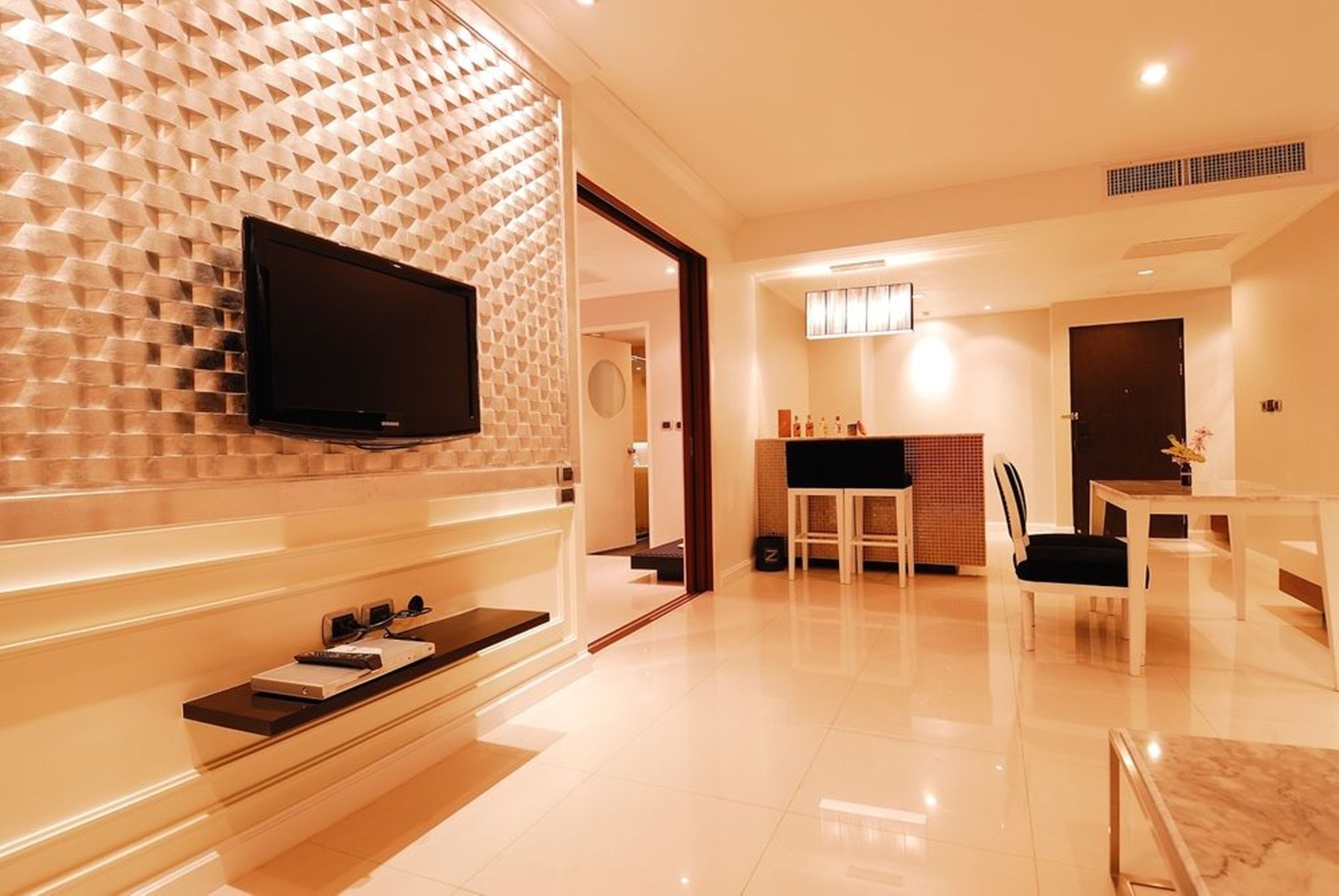 Un hall d’hôtel moderne doté d’un téléviseur à écran plat fixé sur un mur texturé, d’un comptoir de réception et d’un espace repas avec des chaises et une table.