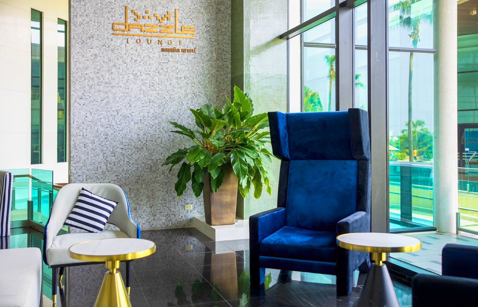 A lounge area with a blue armchair, a white armchair with a striped pillow, and a potted plant.