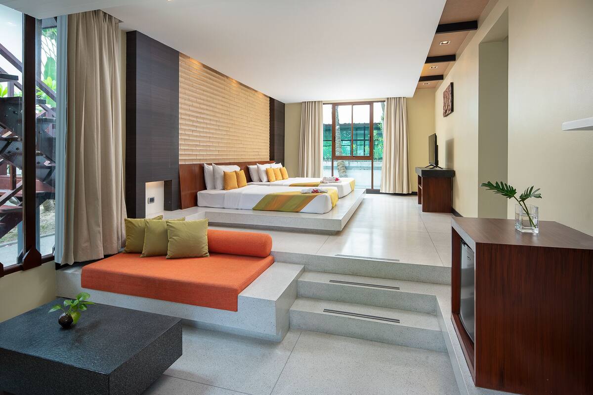A modern hotel room with a large bed, a sofa, a desk, and a view of the outdoors.