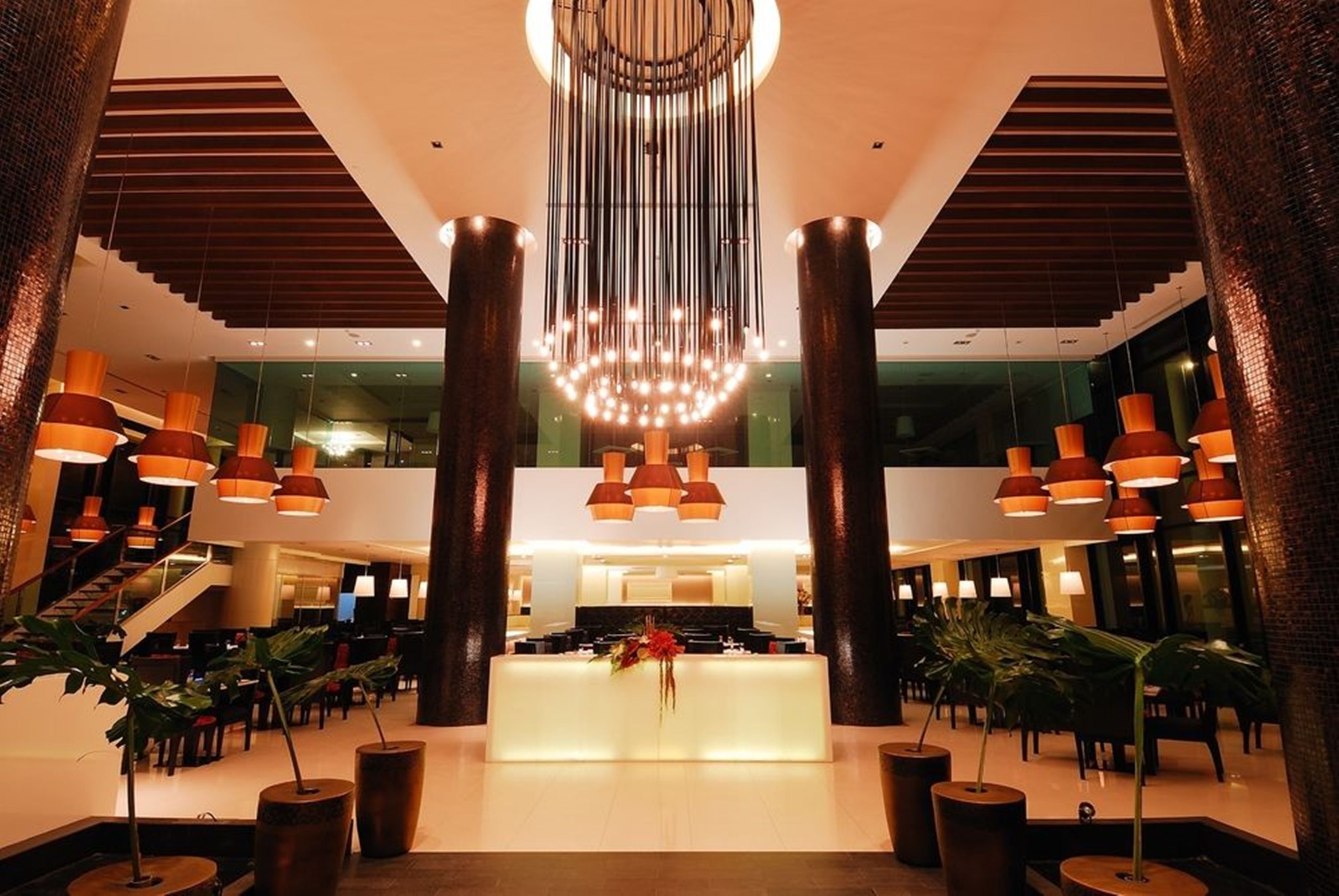 A spacious lobby with a central reception desk, large pillars, and hanging pendant lights.