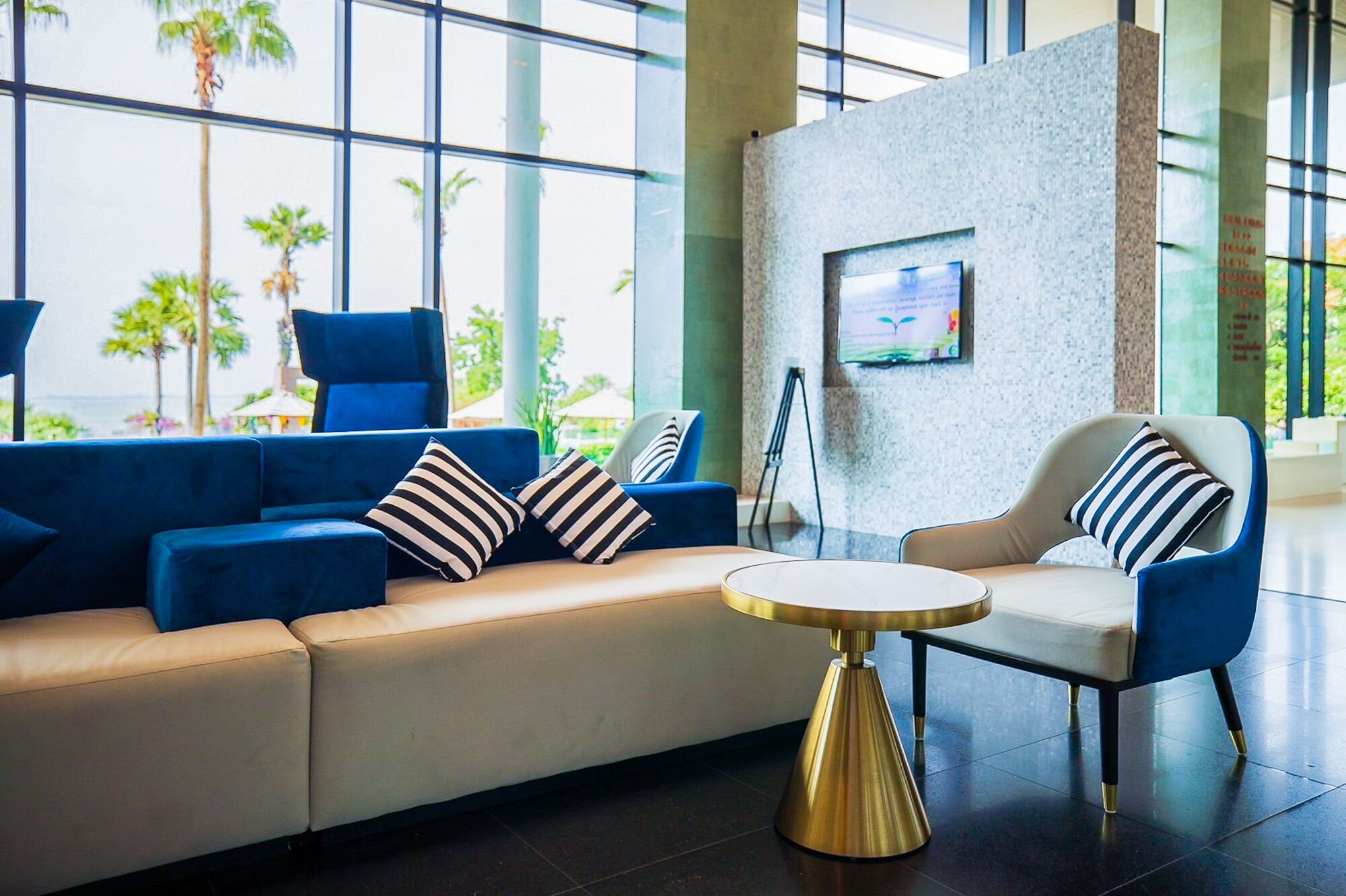 Een moderne lobby met een blauwe bank, een ronde gouden tafel en een beige fauteuil.