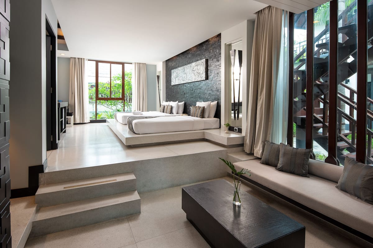 A modern bedroom with a large bed, a sofa, and a coffee table. There is a staircase leading to an outdoor area.