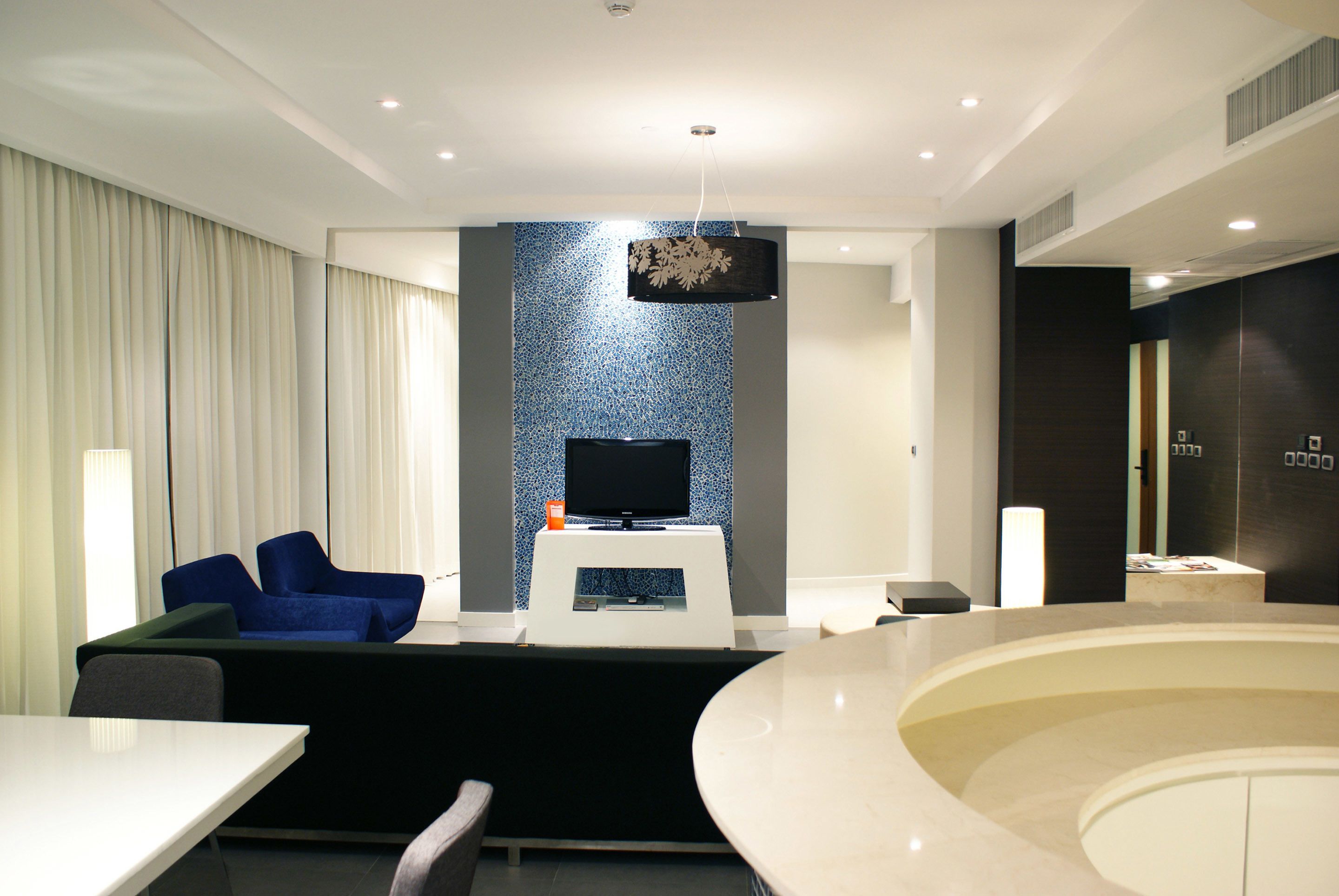 Une chambre d’hôtel moderne dotée d’une télévision à écran plat, d’un canapé, d’une table à manger et d’une baignoire au design incurvé unique.