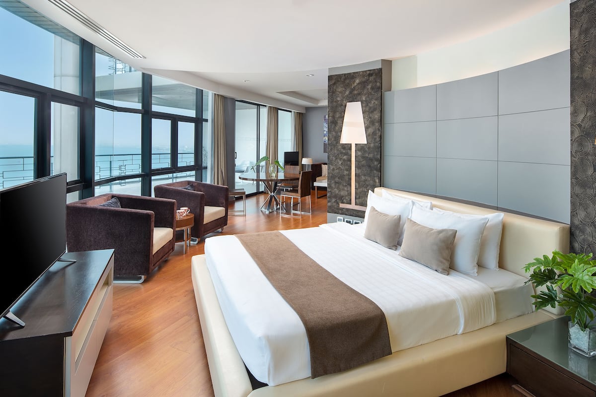 A modern hotel room with a large bed, a desk, a TV, and a view of the ocean.