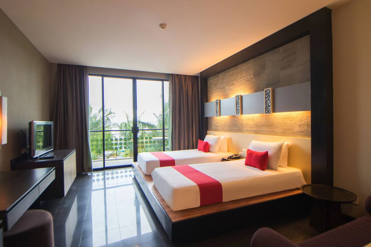 A hotel room with two beds, a TV, a desk, and a view of the outdoors.
