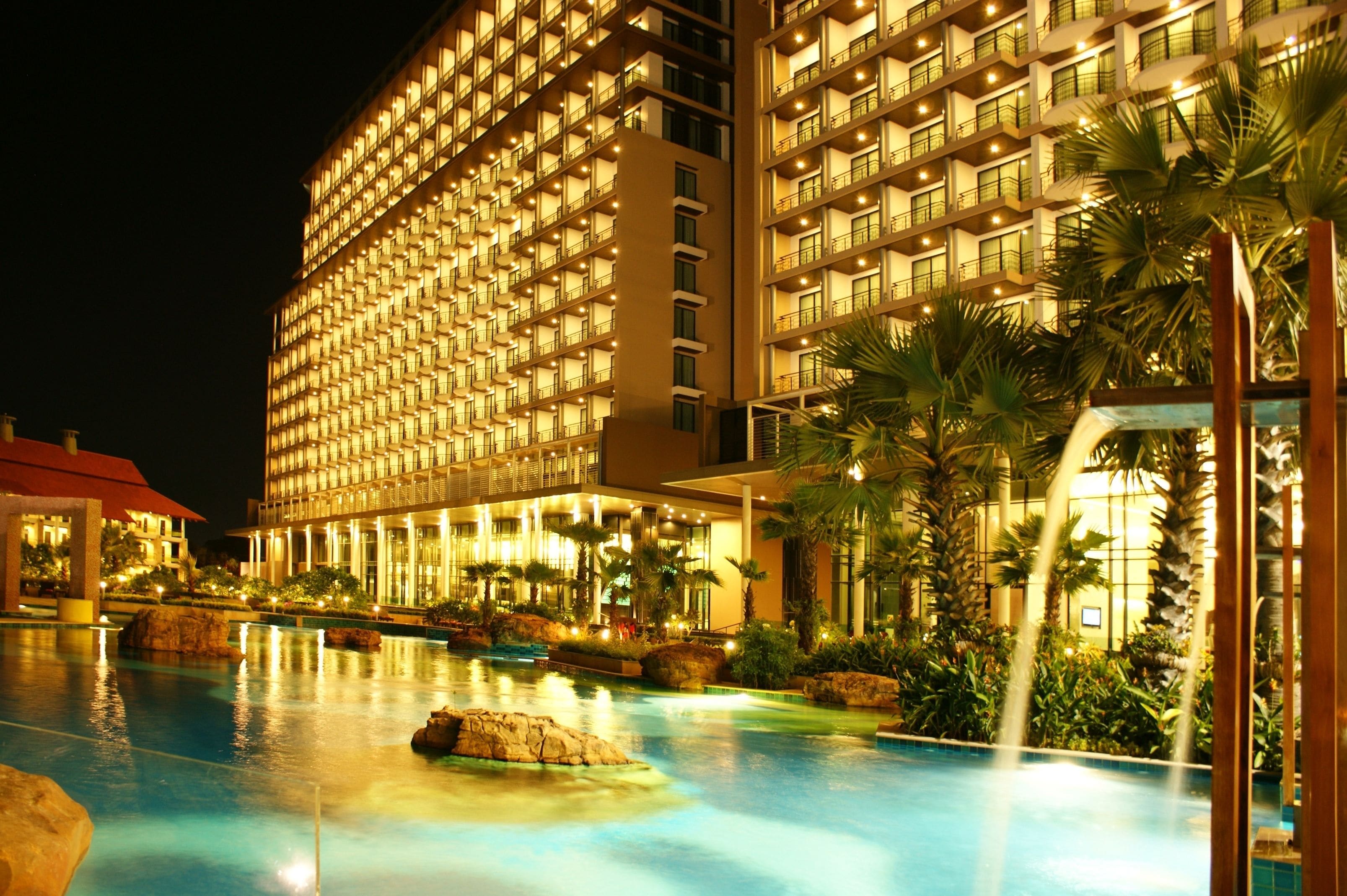 A hotel with multiple floors, a swimming pool, and palm trees.