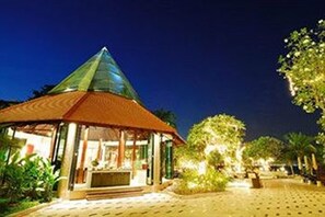 A hotel with a glass pyramid structure, a covered entrance, and a well-lit outdoor area with trees. - The Zign Hotel (Pattaya)