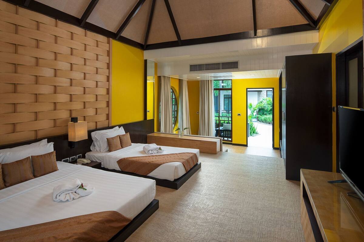 A hotel room with two beds, a TV, and a balcony with plants.